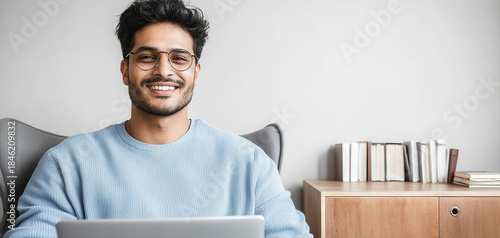 Smiling man using laptop at home office. Modern remote work lifestyle image for business, technology, freelance and online communication themes.