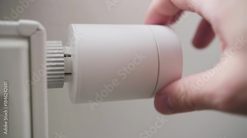 Man rotating radiator thermostat to raise heating level in the room.