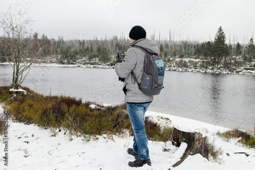 Person taking pictures near snowy lake in winter forest