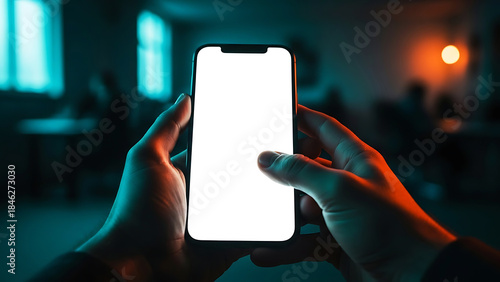 Hand holding smartphone iphone with a blank white screen mockup in a dark room with neon lights