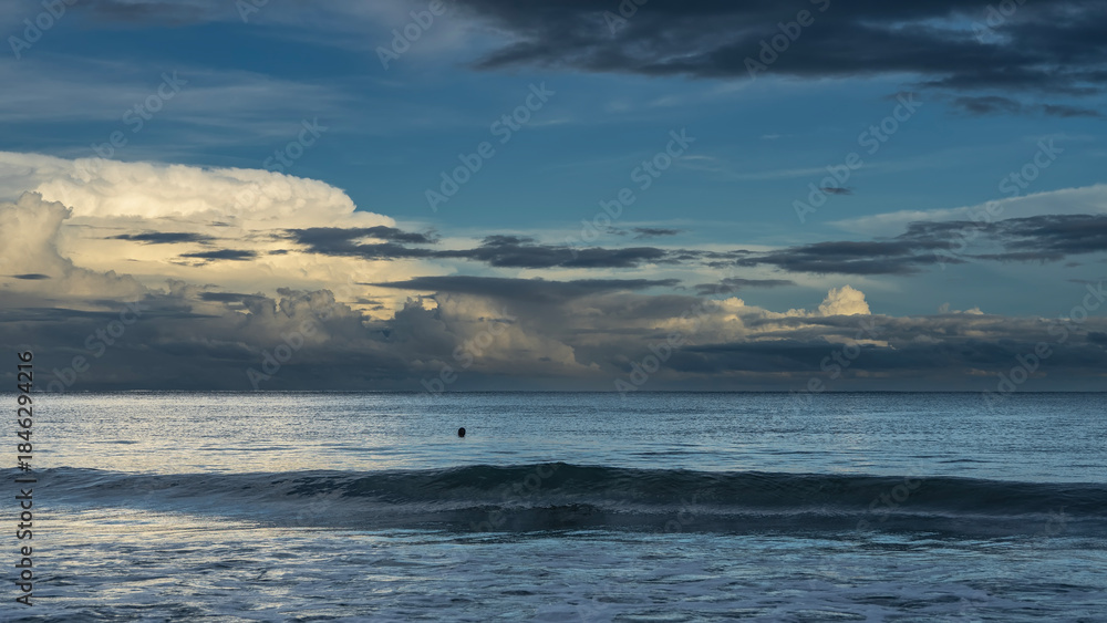 Obraz premium Early morning. The ocean waves are rolling towards the shore. The head of a floating man is visible in the sea. The clouds in the blue sky are illuminated with golden light. Malaysia. Borneo.