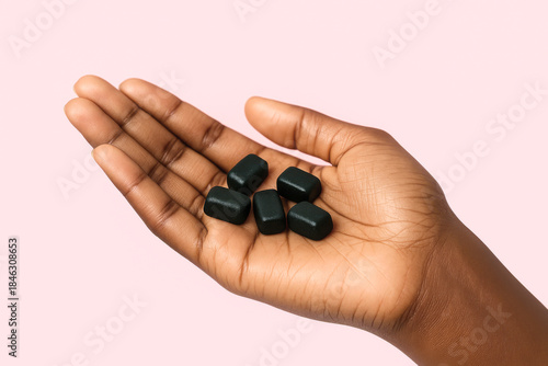 person's hand displaying a handful of dark green rectangular vitamin gummies representing health wellness and self-care on a light pink background
