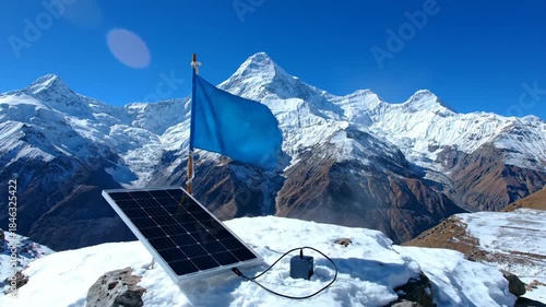 Solar panel and flag on snowy mountain peak under clear blue sky