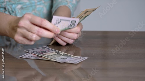 female hands counting cash on table, closeup of sorting and stacking bills with floral sleeve visible, calm