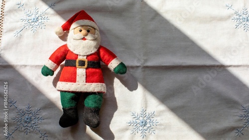 Santa doll rests on a white tablecloth with snowflakes during the holiday season in a cozy indoor setting