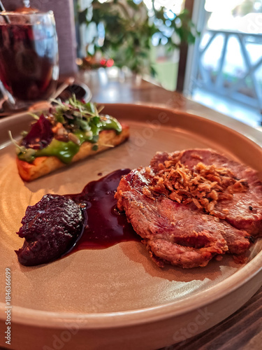 Gourmet roasted pork steak served with crispy onions, sauce and vegetable garnish on elegant plate in modern restaurant. Fine dining meat entrée, European cuisine, food photography with shallow depth