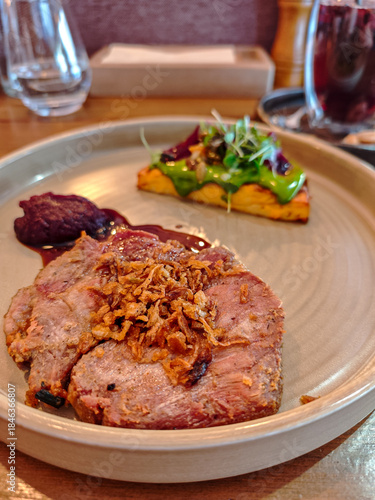 Gourmet roasted pork steak served with crispy onions, sauce and vegetable garnish on elegant plate in modern restaurant. Fine dining meat entrée, European cuisine, food photography with shallow depth 
