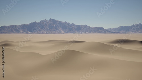 Golden sand dunes roll across the horizon, with mountains gently rising in the distance. The bright blue sky contrasts beautifully with the warm tones of the desert. A serene and tranquil scene.