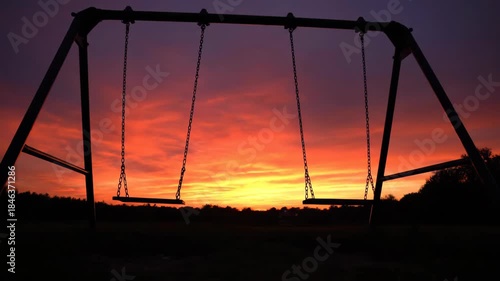 Swing set silhouette against a vivid sunset sky, peaceful evening