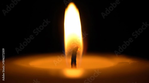 Burning candle with bright flame against a dark background detail