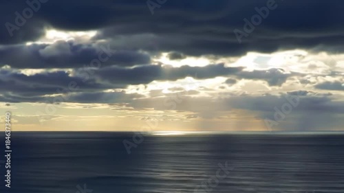 Sunlight breaks clouds over ocean horizon; seascape scenery for backgrounds