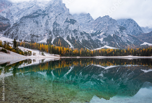 Autumn forest reflected in Lago di Braies surrounded by the Dolomites