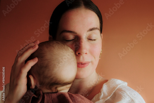 Mother holding baby close with eyes closed in warm light