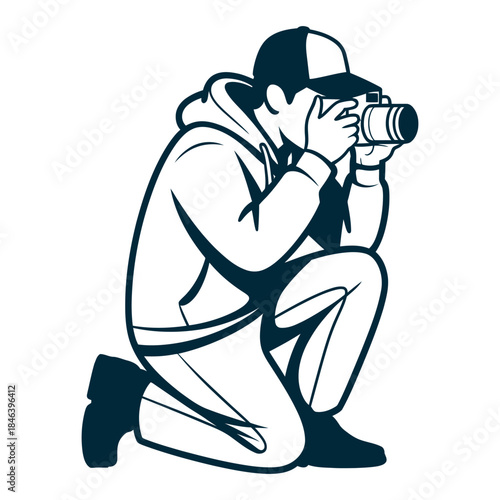 A person wearing a baseball cap and hoodie kneels while taking a photo with a camera.