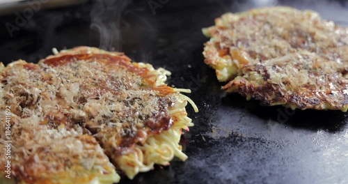 Macro okonomiyaki on a hot teppan in Japan with moving bonito flakes and rising steam, capturing delicate heat driven motion across the surface in a static close cooking view