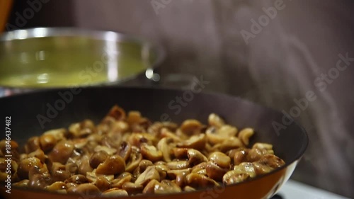 A slow-motion close-up of sliced small porcini mushrooms being fried in a frying pan in a home kitchen. Stirring the mushrooms as they fry by tossing them in the pan.
