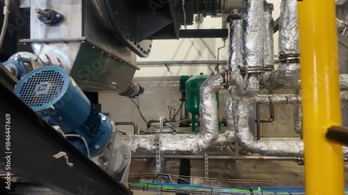 Industrial machinery, insulated pipes, blue motor, green tanks, metal structures, wiring in an abattoir facility. industrial setting featuring complex piping,