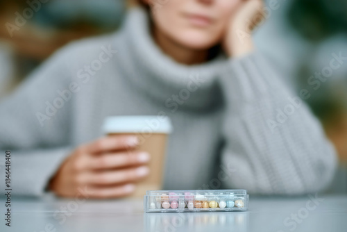 Woman with weekly pill organizer and coffee cup on table, managing daily medication