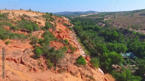Aerial view of the Fairy Stream in Mui Ne: striking red sandstone formations and lush green jungle under a clear blue sky.