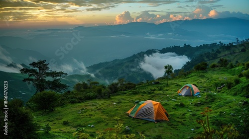 Peaceful camping in a mountainous area by a lake. A tent and a cozy campfire are located among the rocks against the backdrop of beautiful mountains and tall trees.