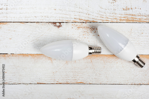 Two LED lamps with E14 sockets lying on a wooden surface.