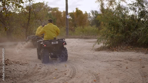 Four riders on AVTs kicking dust through sandy forest trail, yellow jackets, rear follow shot capturing wheel spray, dynamic turning, gravel