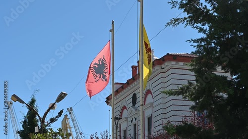 Flags of the Albanian Orthodox Church and Albania flying on flagpoles near a church in Durres, showcasing religion, national identity, and cultural heritage.