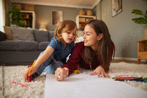 A woman and a young child engage in a fun drawing activity on the floor. They are surrounded by colorful crayons and are enjoying quality time together in a warm, cozy living room.