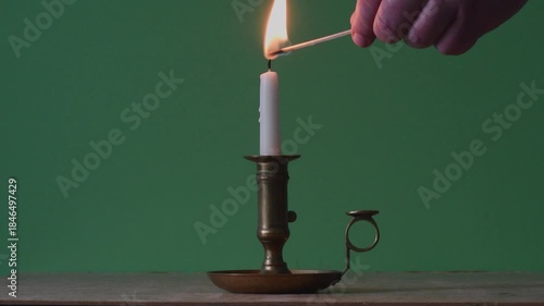 Man in red places a candle in an antique candlestick on the table and lights it with a match
