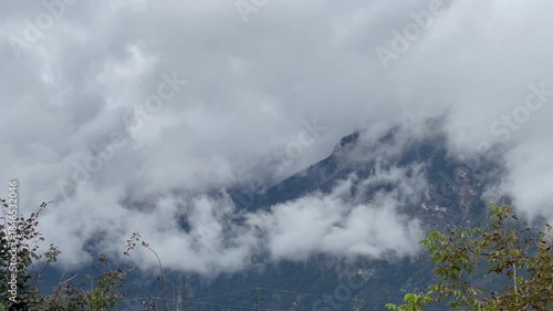 Low clouds moving horizontally across a mountain ridge, briefly revealing dark forested slopes beneath. 