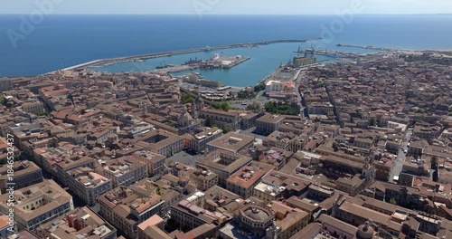 Aerial view of the city of Catania, Sicily, Italy. In the foreground there is the Metropolitan Cathedral of Saint Agatha. In the background, the city port and the Mediterranean Sea on the horizon.