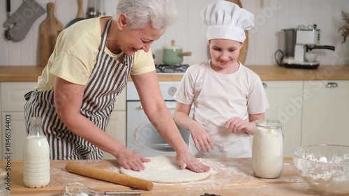 Happy family in kitchen. Grandmother and granddaughter child cook in kitchen together. Grandma teaching kid girl knead dough bake cookies. Household teamwork helping family generations concept