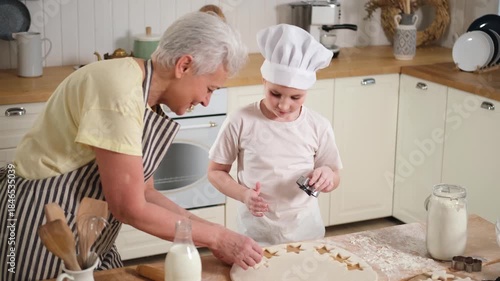 Happy family in kitchen. Grandmother granddaughter child cutting cookies of dough on kitchen table together. Grandma teaching kid girl cook bake cookies. Household teamwork helping family generations