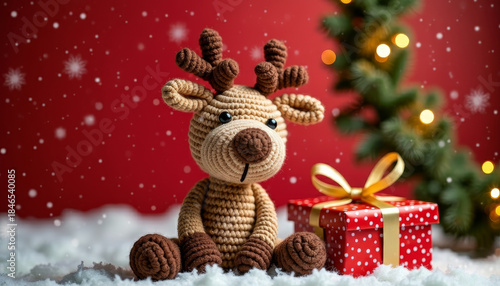 Cute knitted reindeer with gift box on bright red festive Christmas background cozy holiday scene
