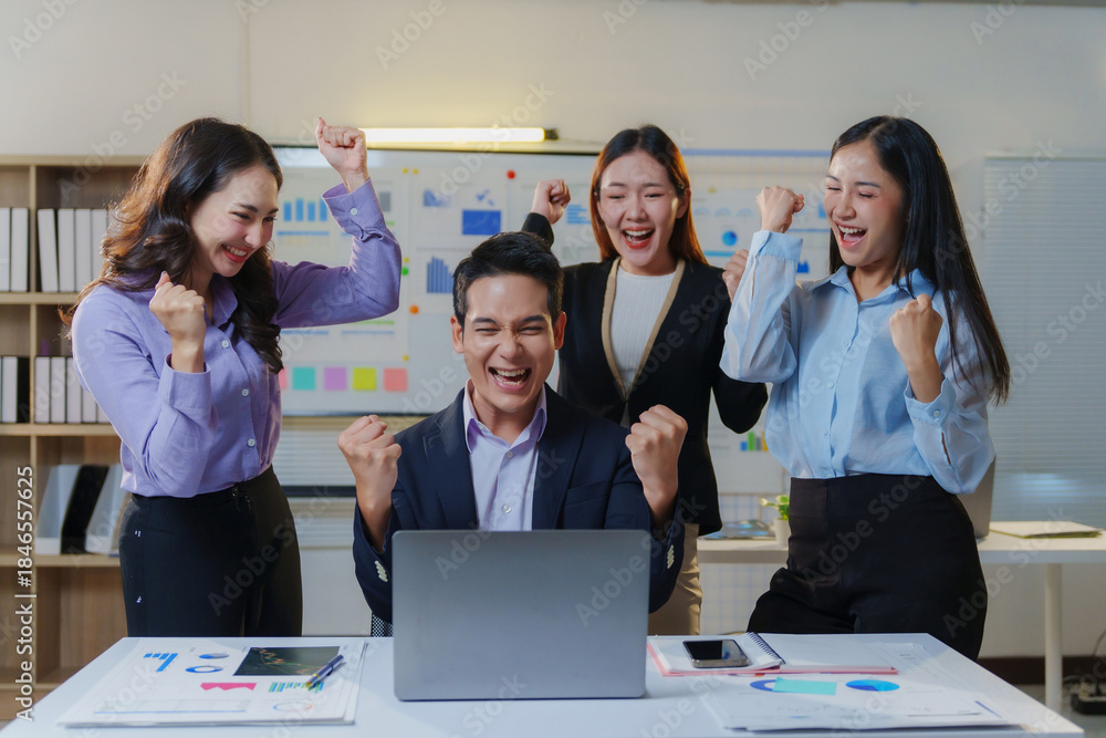 Obraz premium Happy Asian business team celebrating success in the office, cheering and raising fists, showing concept of goal achievement