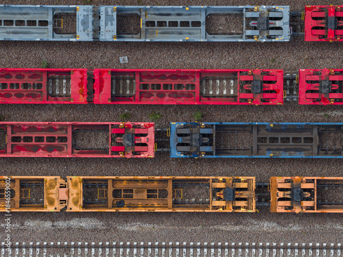 Aerial view of colorful train cars parked on parallel tracks, a geometric dance of steel and hues, contrasting with the earthy tones of the gravel, Trieste, Italy.