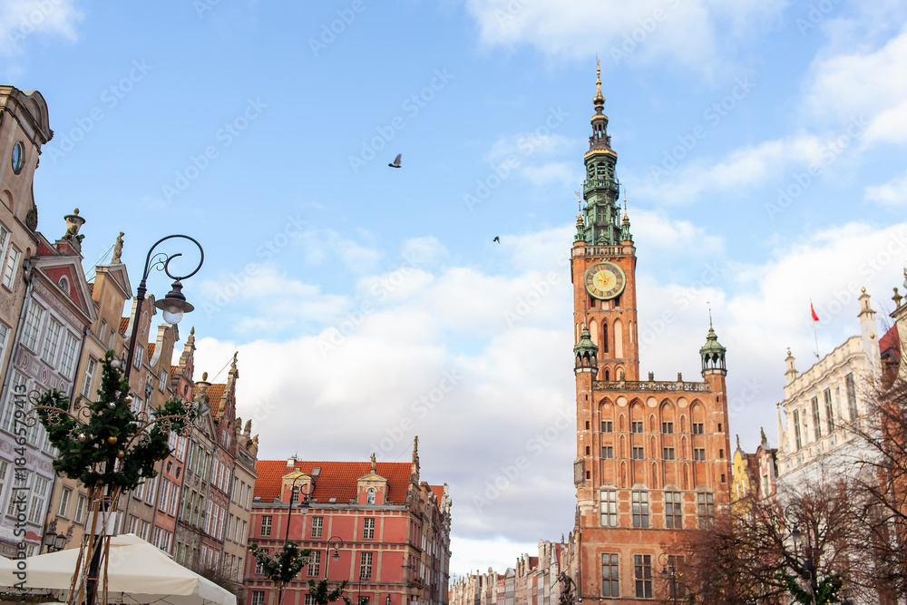 Obraz premium A clock tower stands tall in city sqare. Street in an Old town and Town Hall in Gdansk, Poland. Panoramic view. Historical city of Gdansk (Danzig), Poland, Europe.