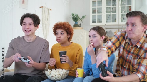 Home party. Cheerful group of friends playing video games at home. Happy diverse group buddies having fun together indoor. Friendship leisure entertainment concept. Young best friends enjoying weekend
