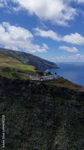 Aerial 4K drone footage of dramatic coastal cliffs and lighthouse viewpoint on Madeira island, overlooking the deep blue Atlantic Ocean and rugged shoreline in clear daylight.