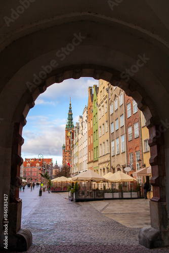 A walk along the cobblestone street in Gdansk, Poland. Colorful buildings line the path with a tall tower of City Hall visible in the background. Dlugi Targ, Long Market