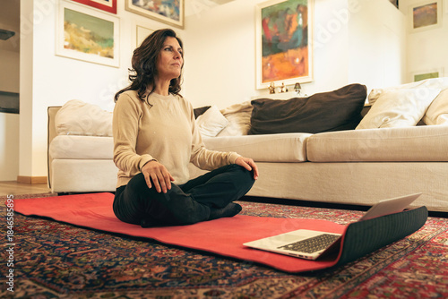 Bilde på lerret Middle aged woman practicing mindfulness at home with laptop on yoga mat