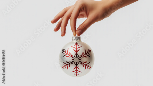 Hand holding a silver christmas ornament with red snowflake pattern