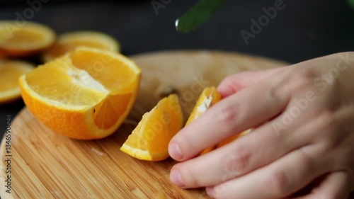 Close up of female hand cutting a fresh orange fruit on wooden cutting board 