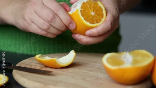 Close up of female hand cutting a fresh orange fruit on wooden cutting board 