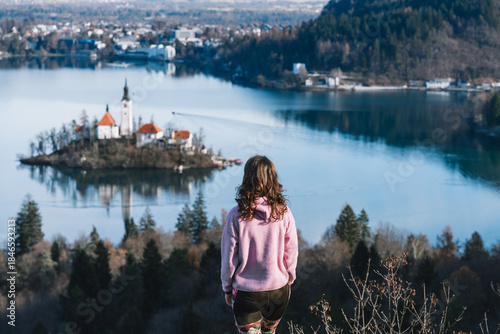 Canvas-taulu Woman enjoy the scenic view of Bled Lake with Church on Island in middle of lake framed with mountain peaks covered in snow
