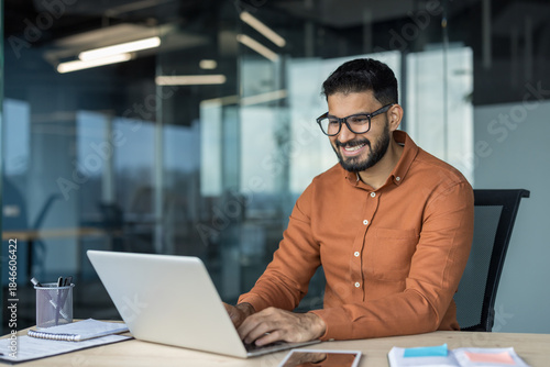Obraz na płótnie Young smiling indian businessman engaging with his laptop while happily working