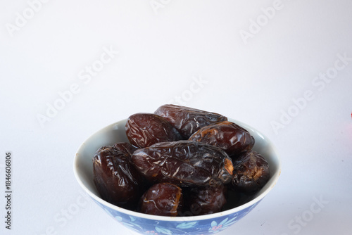 Bowl filled with dark brown dates on white background