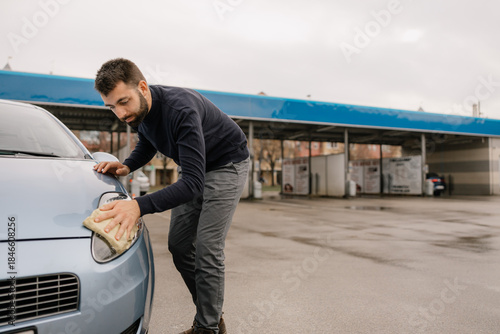 Male worker polishing car window during wash service