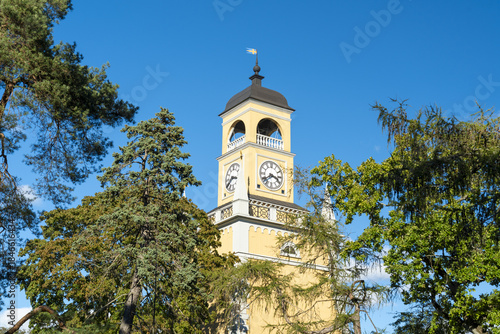 View of Amiralitetsklockstapeln clock tower standing tall from below, framed by vibrant green foliage under blue sky, Karlskrona, Blekinge County, Sweden.