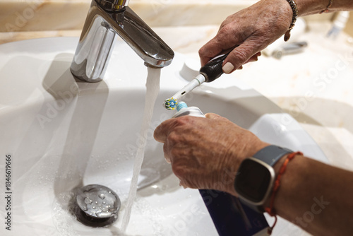 Senior woman preparing electric toothbrush at bathroom sink